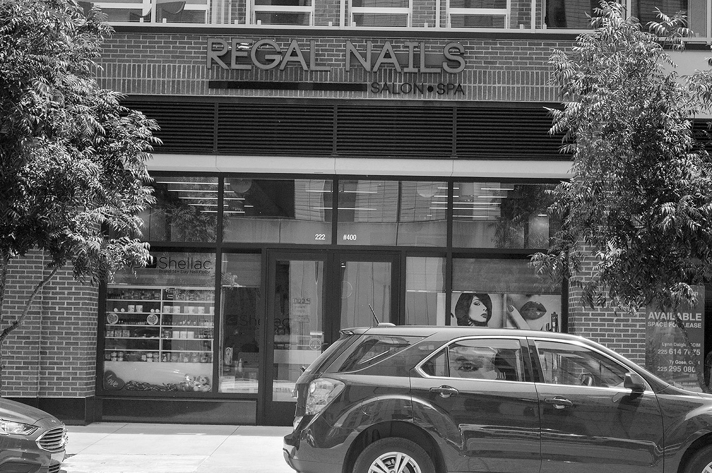 Black and white photo of the Regal Nails Store in Baton Rouge with a car parked in front.